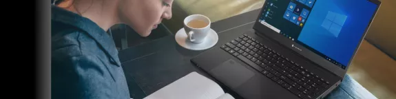 Woman writing at desk with notepad coffee and laptop